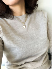 A heart-shaped charm gold necklace featuring Mother of Pearl shell encrustation, suspended on a paperclip chain.