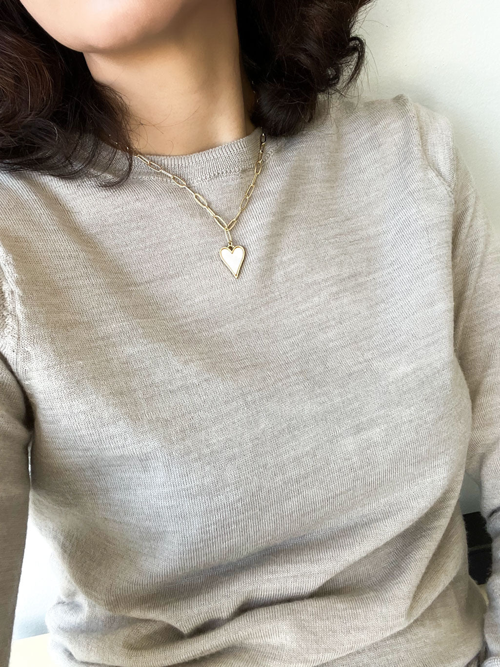 A heart-shaped charm gold necklace featuring Mother of Pearl shell encrustation, suspended on a paperclip chain.