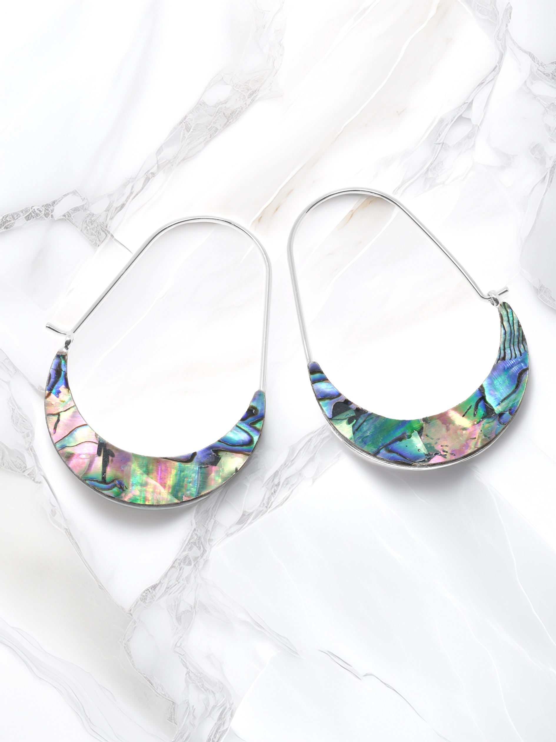A pair of crescent-shaped hoop earrings featuring iridescent abalone shell inlays with vibrant shades of green, blue, purple, and pink. The earrings are set on delicate silver-tone wire hoops.