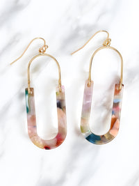 A pair of oval resin drop and dangle earrings with gold-tone hooks and frames. The U-shaped resin pendants feature a multicolored, marbled design in soft pastel and vibrant hues, including pink, blue, green, and peach.