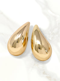 A close-up of gold puffy teardrop hollow bold earrings, showcasing their modern and minimalist design. The earrings make a statement with their sleek metal construction and distinctive shape.