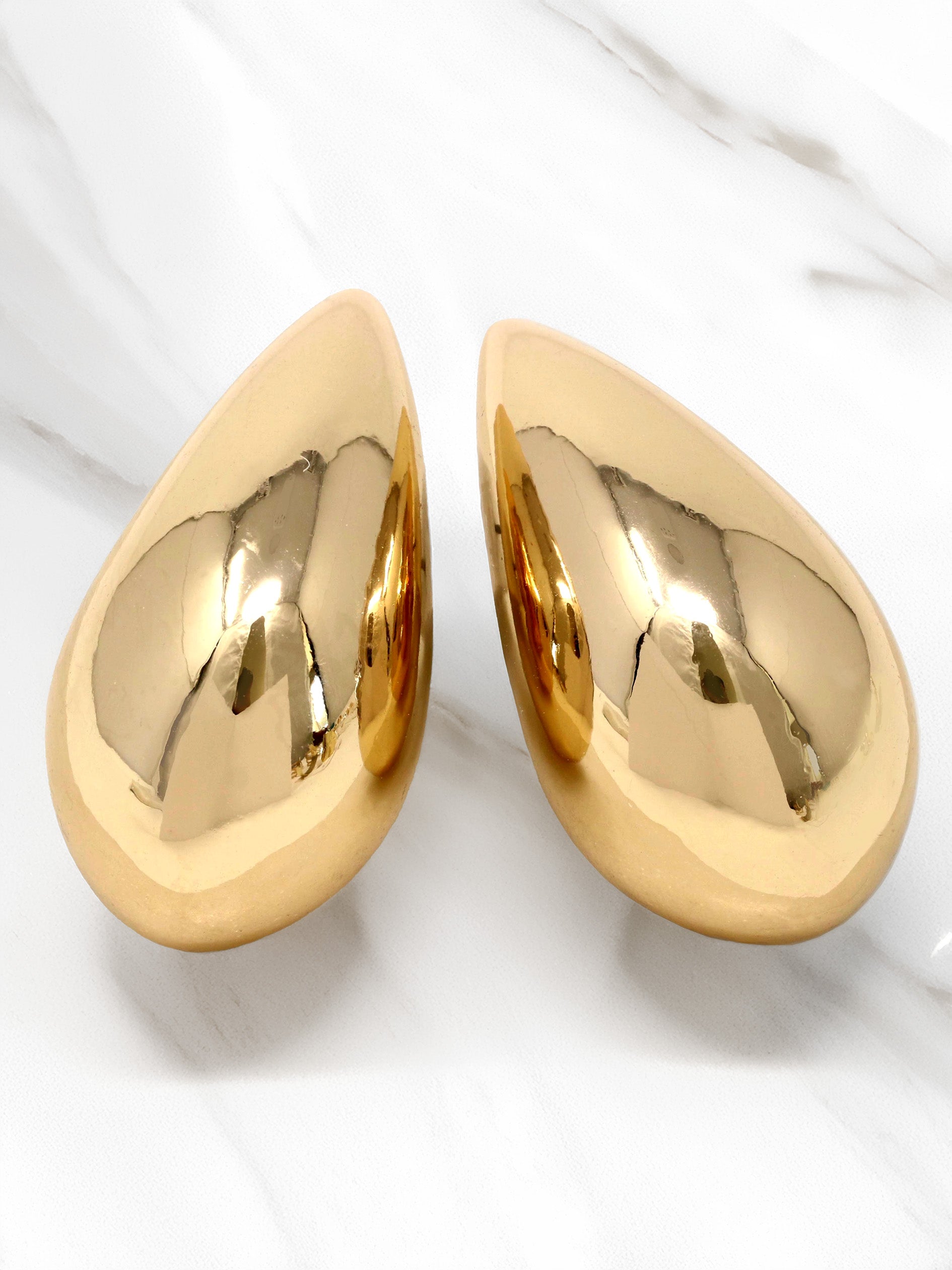 A close-up of gold puffy teardrop hollow bold earrings, showcasing their modern and minimalist design. The earrings make a statement with their sleek metal construction and distinctive shape.