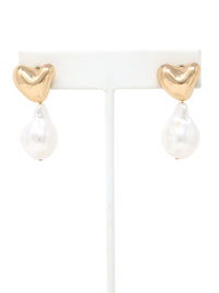 A pair of elegant earrings featuring polished gold-tone puffy heart studs with dangling irregular baroque pearls. The earrings are displayed on a white jewelry stand against a clean background, showcasing their modern yet timeless design.