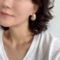 A close-up of gold puffy teardrop hollow bold earrings, showcasing their modern and minimalist design. The earrings make a statement with their sleek metal construction and distinctive shape.