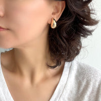 A close-up of gold puffy teardrop hollow bold earrings, showcasing their modern and minimalist design. The earrings make a statement with their sleek metal construction and distinctive shape.