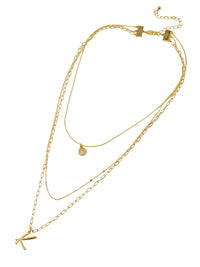 A three-layered gold necklace featuring a script initial charm and a small circle charm paved with stones.