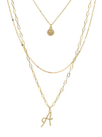 A three-layered gold necklace featuring a script initial charm and a small circle charm paved with stones.