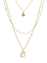 A three-layered gold necklace featuring a script initial charm and a small circle charm paved with stones.