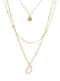 A three-layered gold necklace featuring a script initial charm and a small circle charm paved with stones.