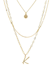 A three-layered gold necklace featuring a script initial charm and a small circle charm paved with stones.