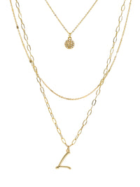 A three-layered gold necklace featuring a script initial charm and a small circle charm paved with stones.