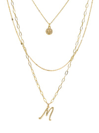A three-layered gold necklace featuring a script initial charm and a small circle charm paved with stones.
