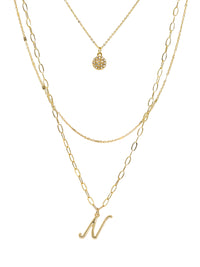 A three-layered gold necklace featuring a script initial charm and a small circle charm paved with stones.