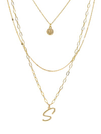 A three-layered gold necklace featuring a script initial charm and a small circle charm paved with stones.