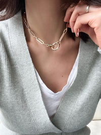 Gold paperclip chain necklace with elongated rectangular links and a circular carabiner lock pendant in the center.