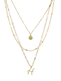 A three-layered gold necklace featuring a script initial charm and a small circle charm paved with stones.