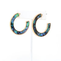 A pair of metal-mounted natural abalone shell hoop earrings. The iridescent abalone shells display beautiful shades of blue, green, black and purple, with a unique natural pattern visible from both sides.