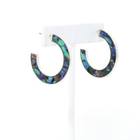 A pair of metal-mounted natural abalone shell hoop earrings. The iridescent abalone shells display beautiful shades of blue, green, black and purple, with a unique natural pattern visible from both sides.