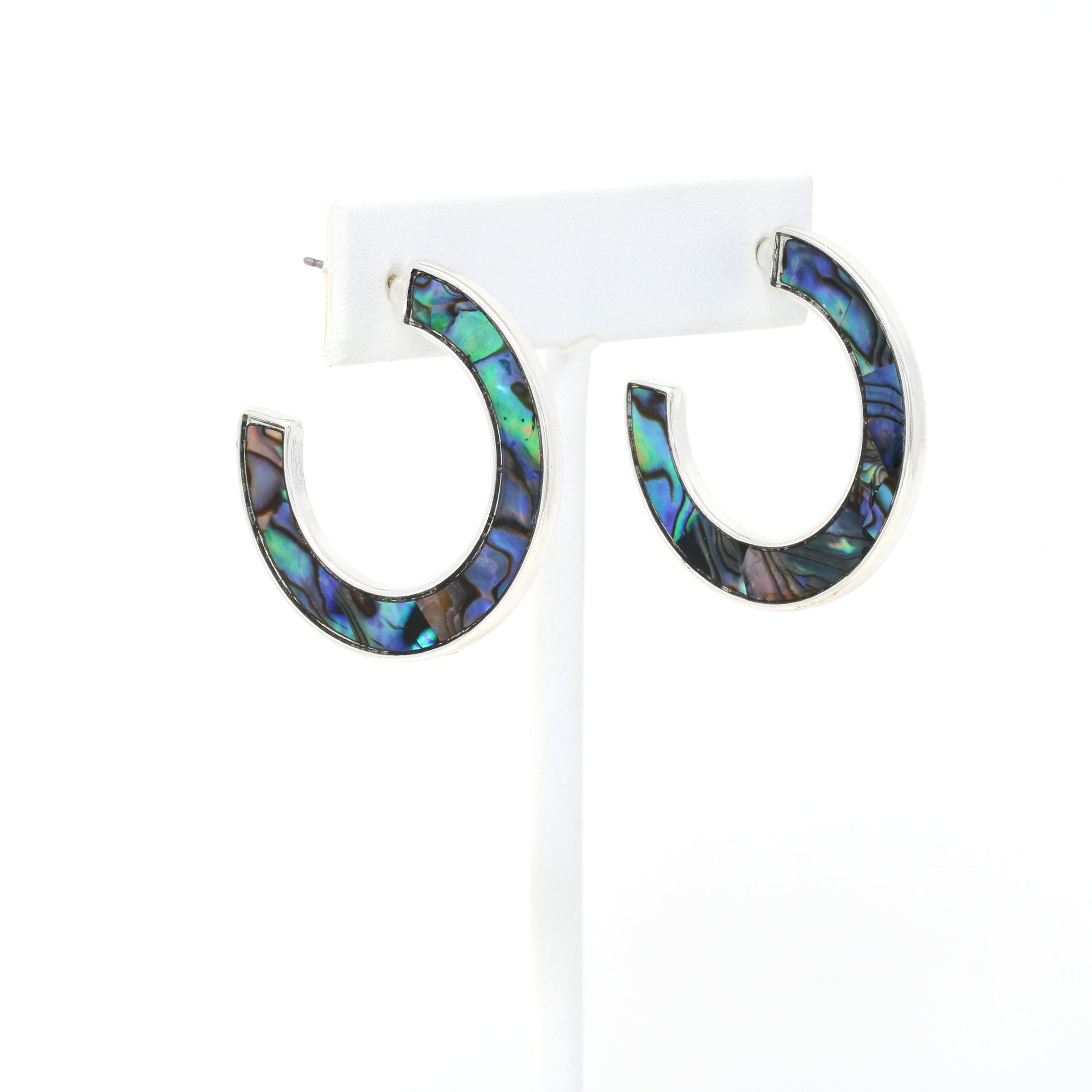 A pair of metal-mounted natural abalone shell hoop earrings. The iridescent abalone shells display beautiful shades of blue, green, black and purple, with a unique natural pattern visible from both sides.