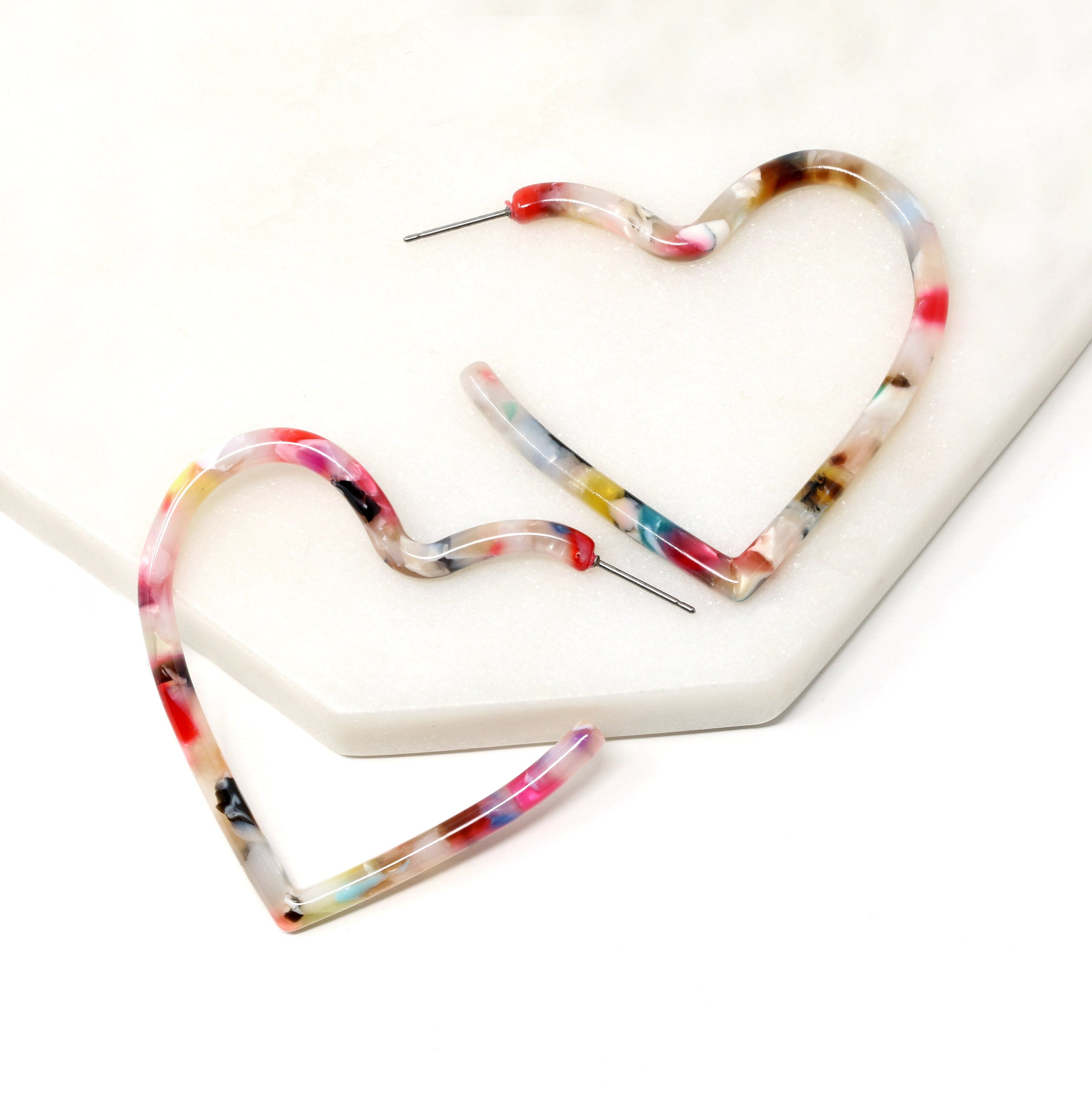 Two heart shaped hoop earrings with a white base and multi-colored swirls of red, pink, blue, yellow, green, and brown.