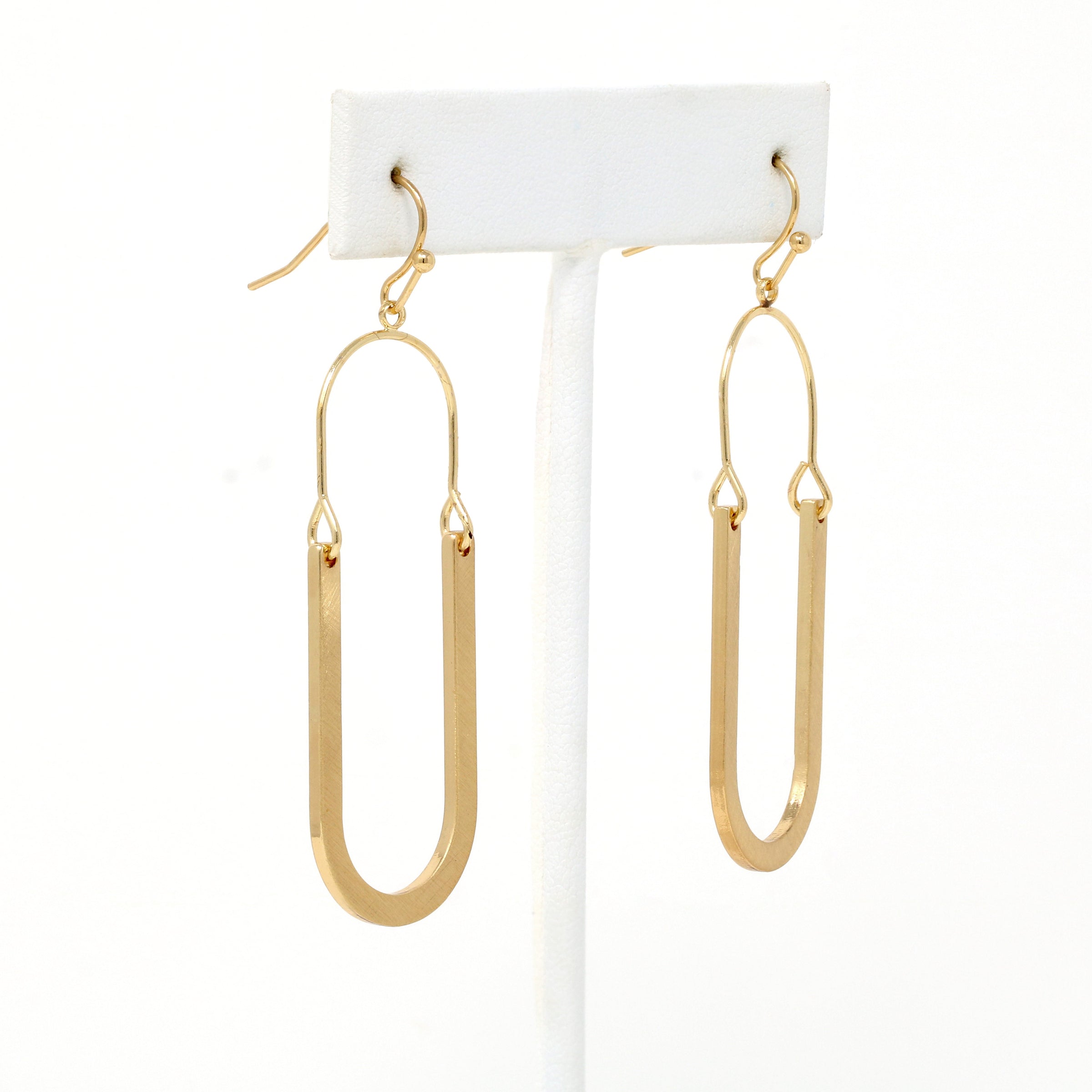 Oval shaped earrings featuring metal drops suspended from gold-plated hooks.