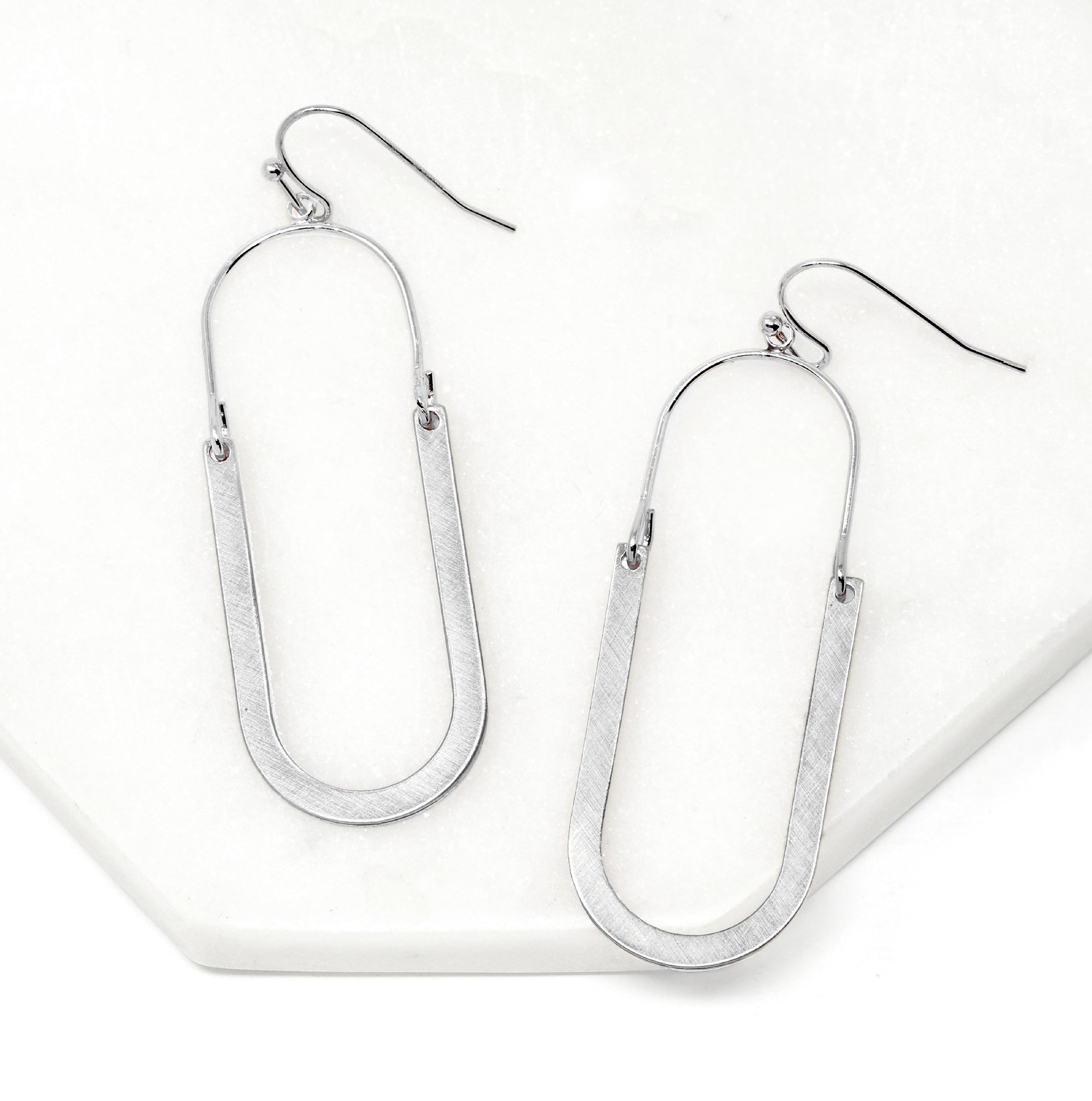 Oval shaped earrings featuring metal drops suspended from silver-plated hooks.