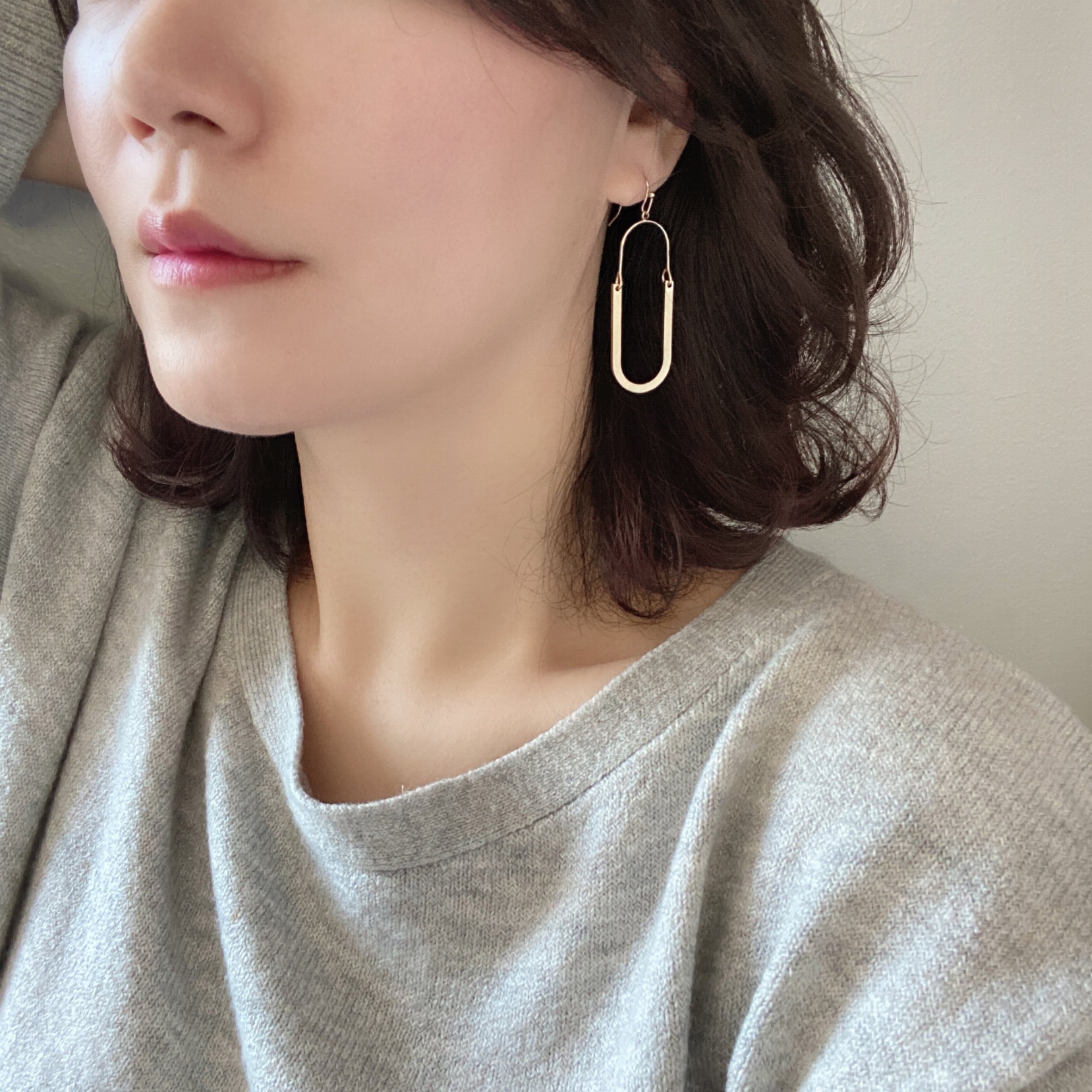 Oval shaped earrings featuring metal drops suspended from gold-plated hooks.
