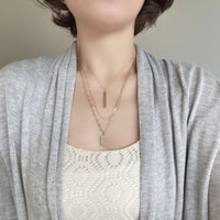 Wearing a modern triple-layered necklace in gold dangled with two bar charms.