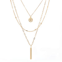 A set of triple layered necklace in gold with a small smiley face and a skinny bar charms.