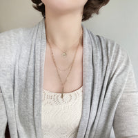 Wearing a set of triple layered necklace in gold with a small smiley face and a skinny bar charms.
