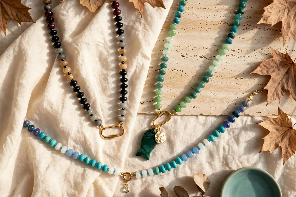 Natural stone beaded necklaces in green, turquoise and rose quartz with gold carabiner clasps, styled on travertine with autumn leaves