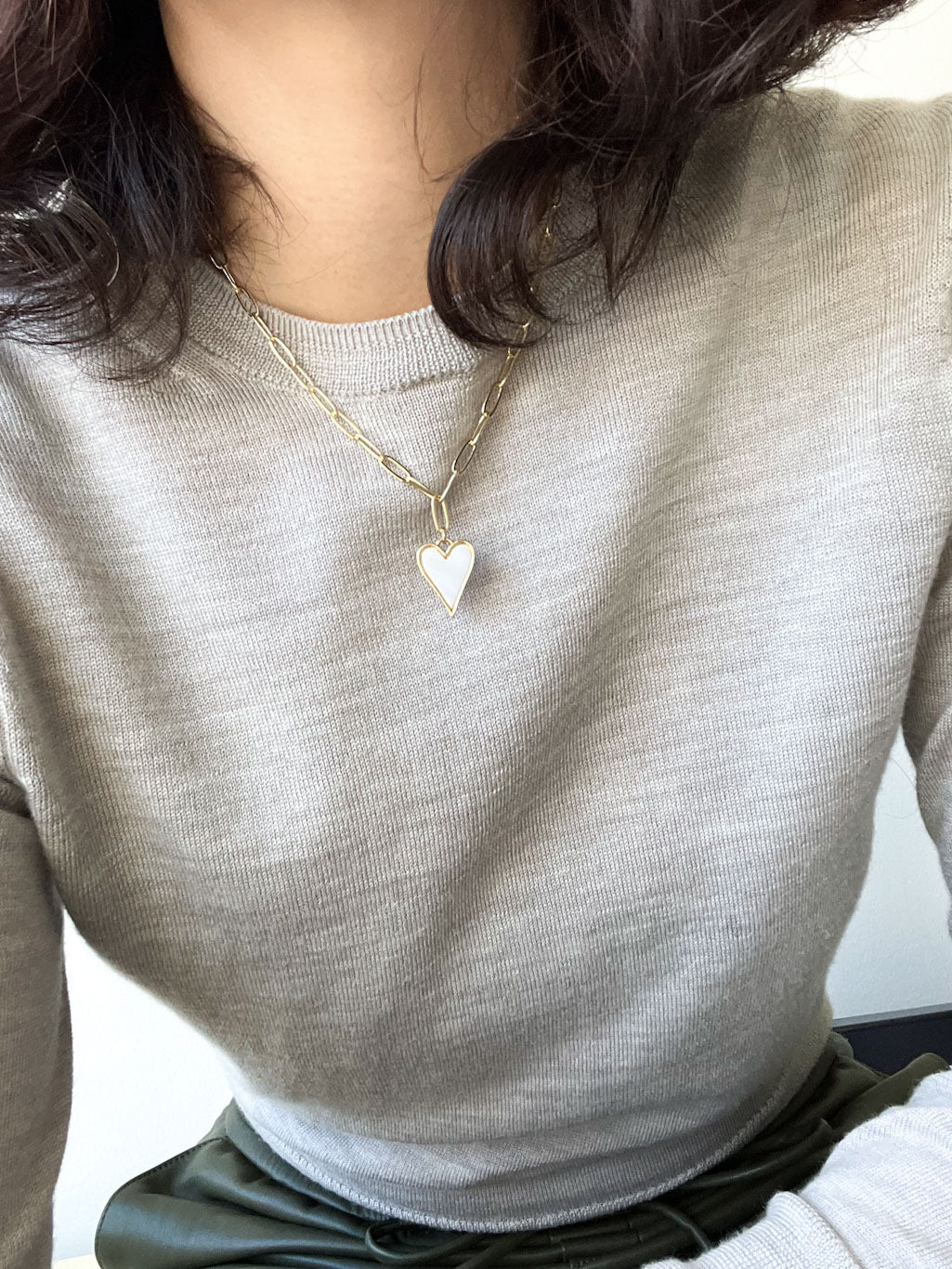 A heart-shaped charm gold necklace featuring Mother of Pearl shell encrustation, suspended on a paperclip chain.