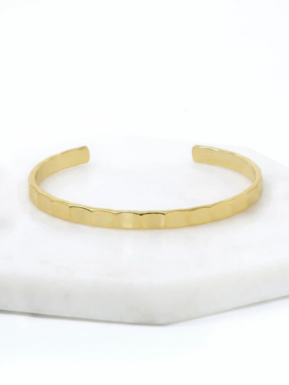 A hammered gold-tone cuff bracelet resting on a white marble surface.