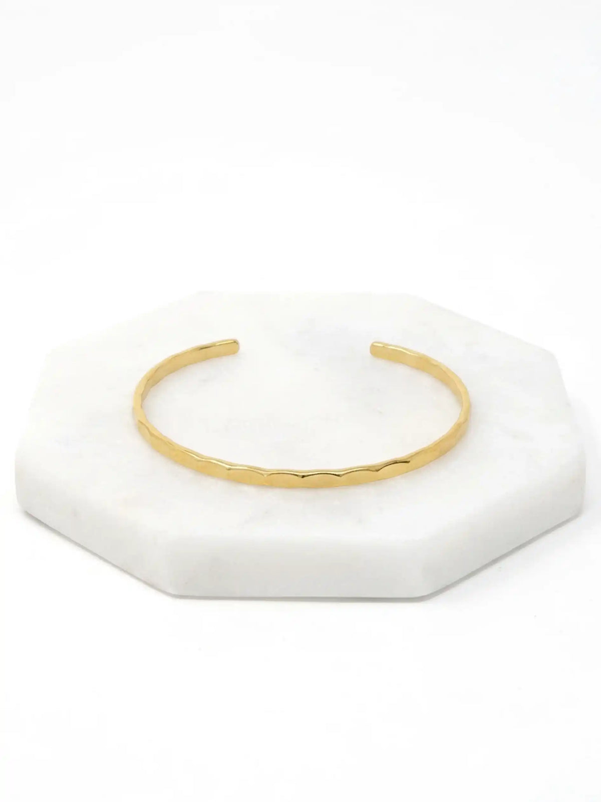 A hammered gold-tone cuff bracelet resting on a white marble surface.