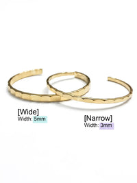 Two overlapping gold-tone cuff bracelets with a textured, scalloped hammered finish, displayed on a clean white background.