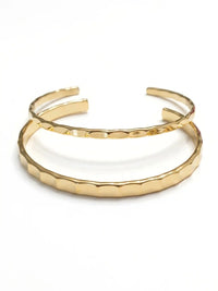 Two overlapping gold-tone cuff bracelets with a textured, scalloped hammered finish, displayed on a clean white background.
