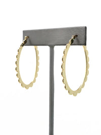 A pair of gold-colored hoop earrings with a scalloped edge design. The earrings are displayed on a gray stand against a white background. The hoops are oval-shaped and have a shiny finish.