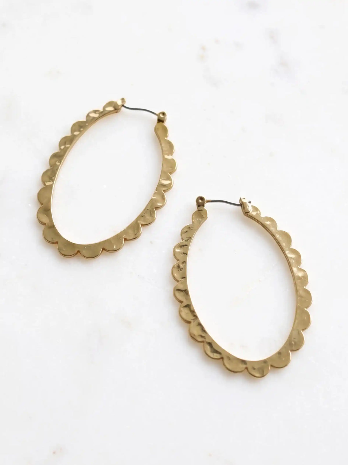 Two gold-colored oval hoop earrings with a scalloped edge design. The earrings are displayed on a white surface. The earrings have a simple hook closure.