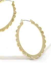 A pair of gold-colored hoop earrings with a scalloped edge design. The earrings are displayed on a gray stand against a white background. The hoops are oval-shaped and have a shiny finish.