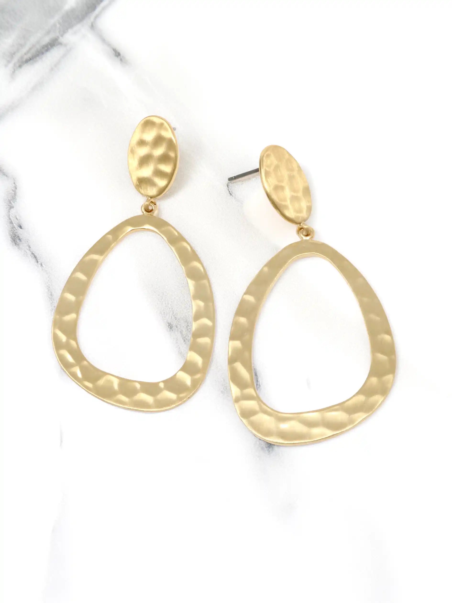 A pair of gold-toned hammered metal earrings with a large oval shape. The earrings have a textured surface and a dangling design.