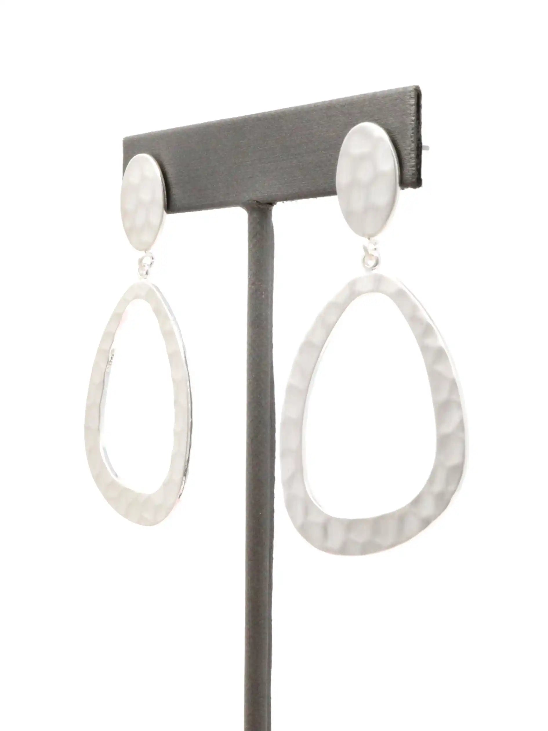 Pair of silver teardrop earrings on a gray earring stand against a white background