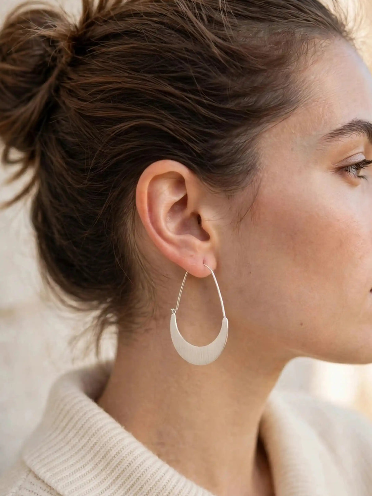 Close-up of a person wearing a gold hoop earring with a neutral background.