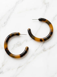 Brown tortoise resin hoop earrings with a marbled pattern of beige, brown, and black, displayed on a white marble background.