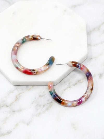 Marbled hoop earrings with a multicolor pattern of pink, blue, purple, and brown, displayed on a white hexagonal marble tray over a white marble surface.