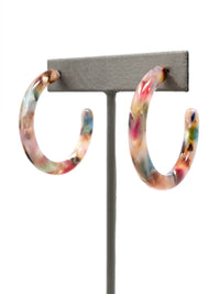 A pair of large marbled acrylic resin hoop earrings in a multicolor pattern of pink, blue, green, and brown, displayed on a gray T-stand against a white background.