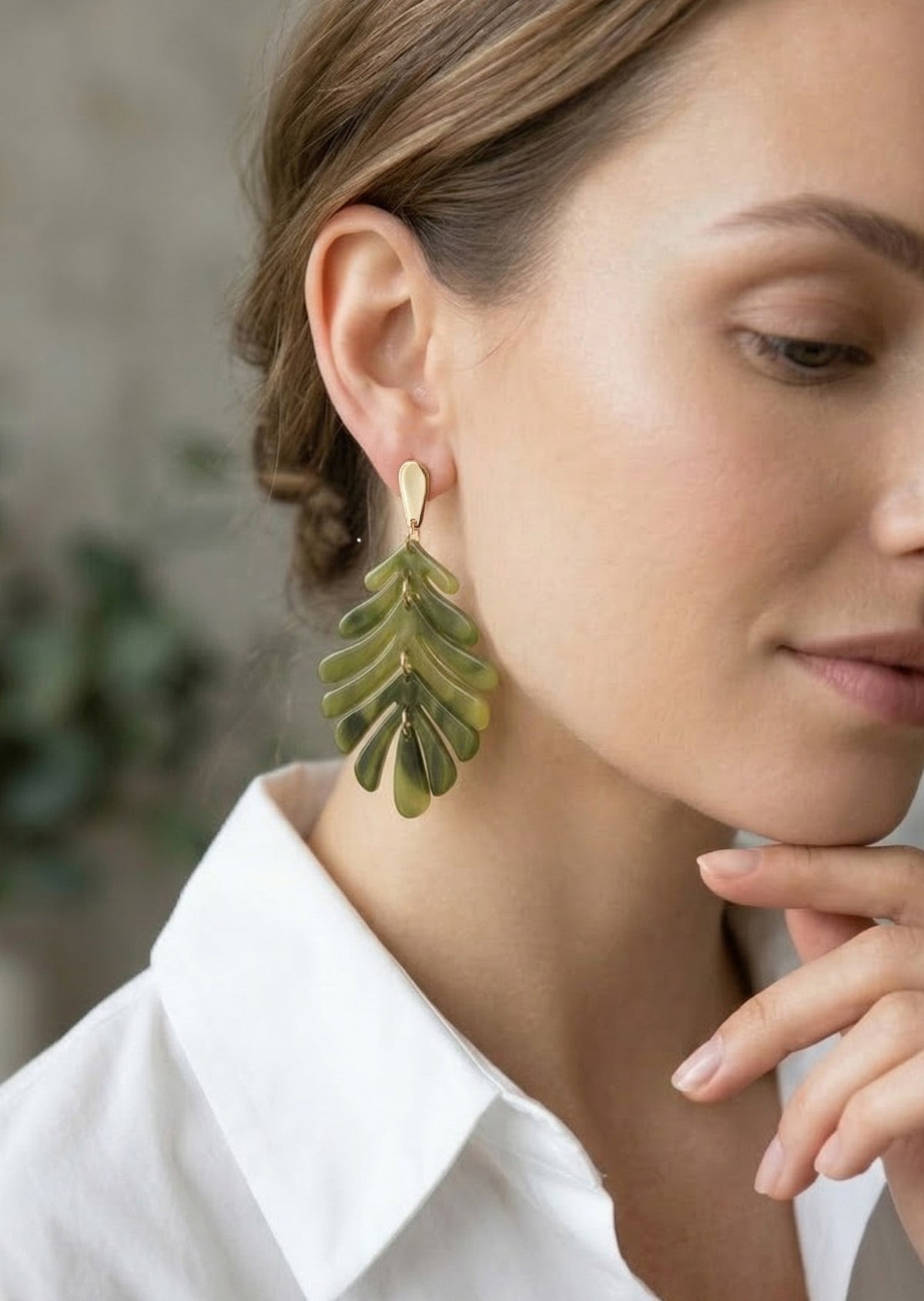 Woman wearing green leaf-shaped earrings with a blurred background