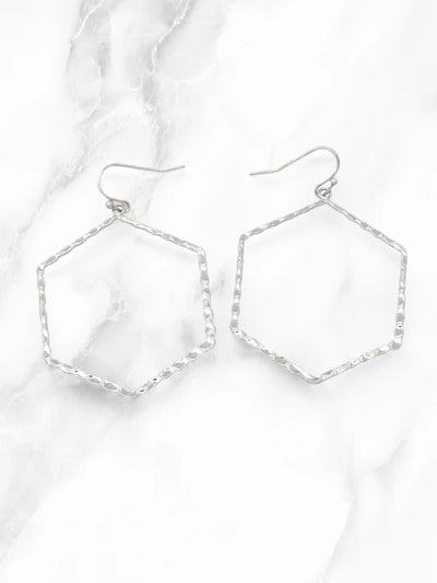 A pair of silver-tone geometric drop earrings with textured hexagonal wire frames and fishhook backings, displayed on a white marble surface.