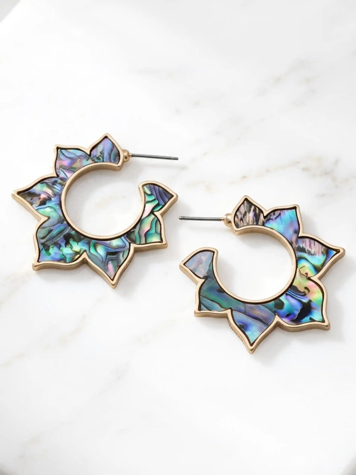 A pair of gold-tone hoop earrings with starburst-shaped abalone shell inlays, displayed on a white marble surface.