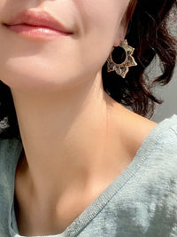 A close-up lifestyle shot of a model wearing a gold-toned geometric floral abalone shell earring with a black circular center.