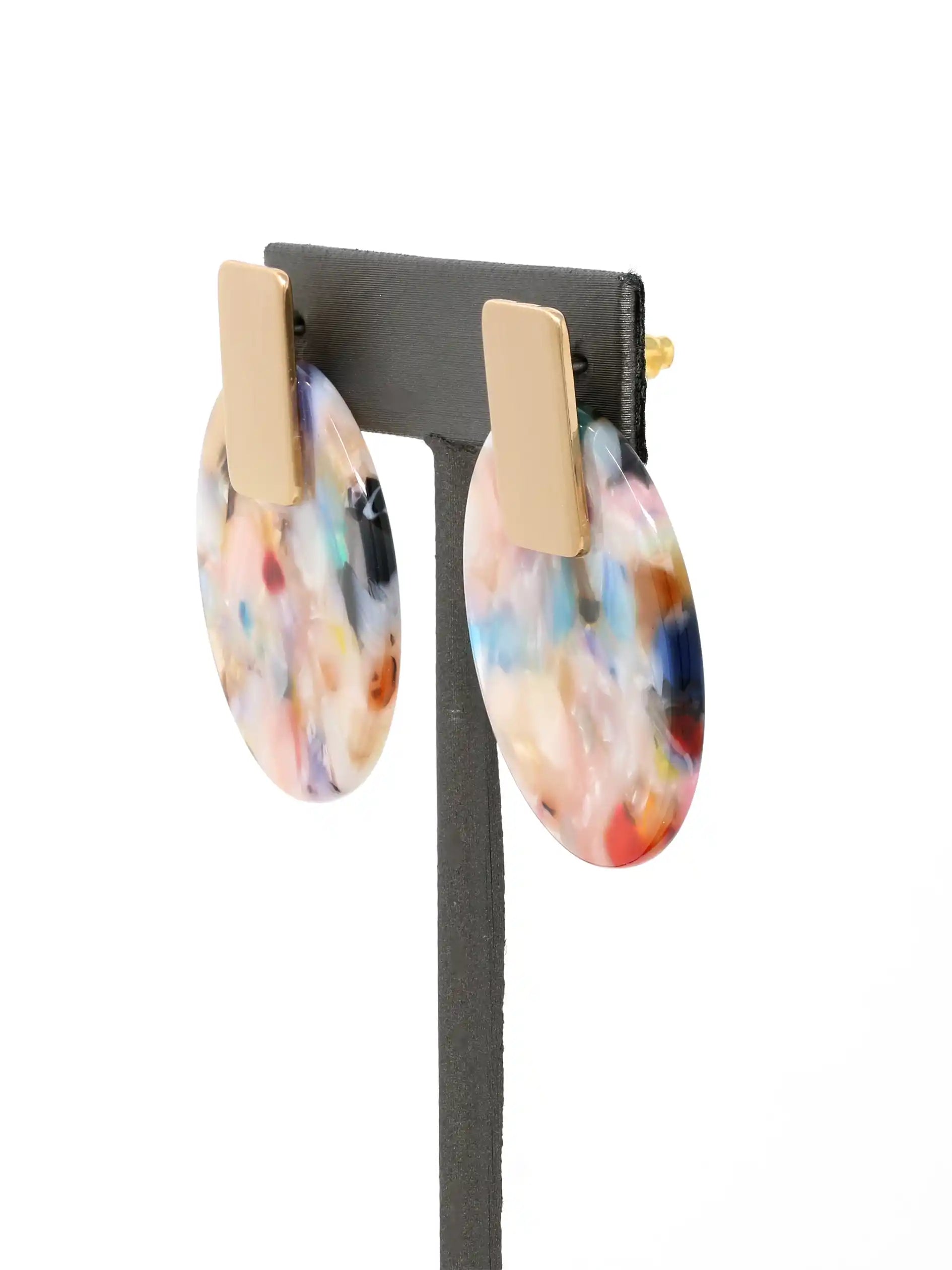 Colorful oval earrings on a black stand with a white background